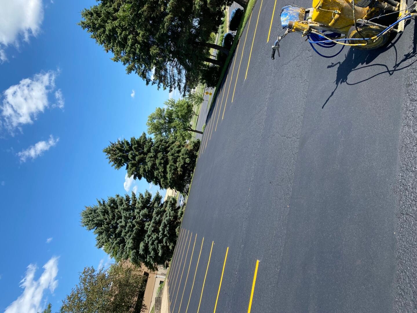 Parking lot striping machine painting yellow lines on fresh sealcoat